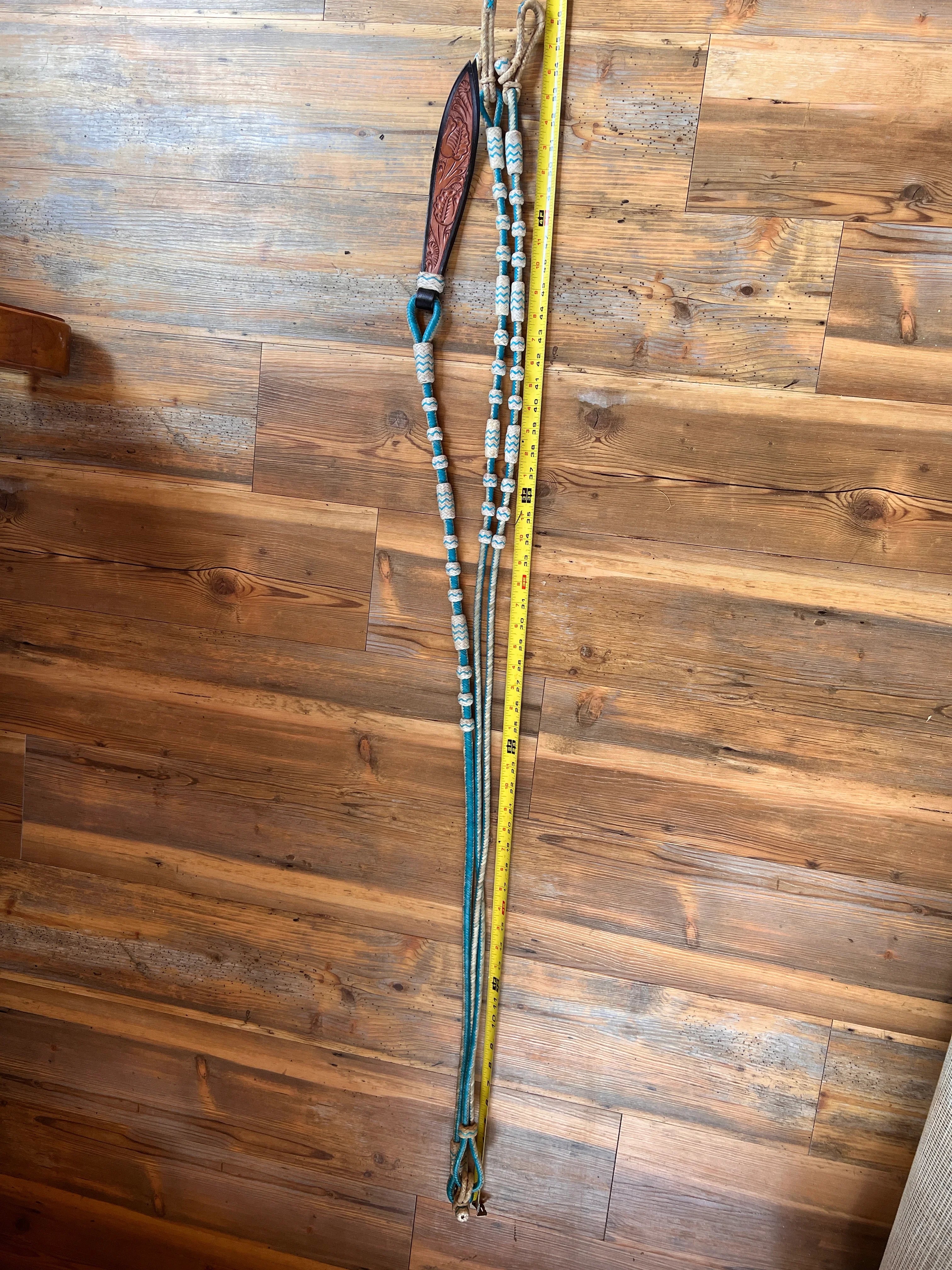Teal and white beaded horse lunge with brown leather handle on Romal reins