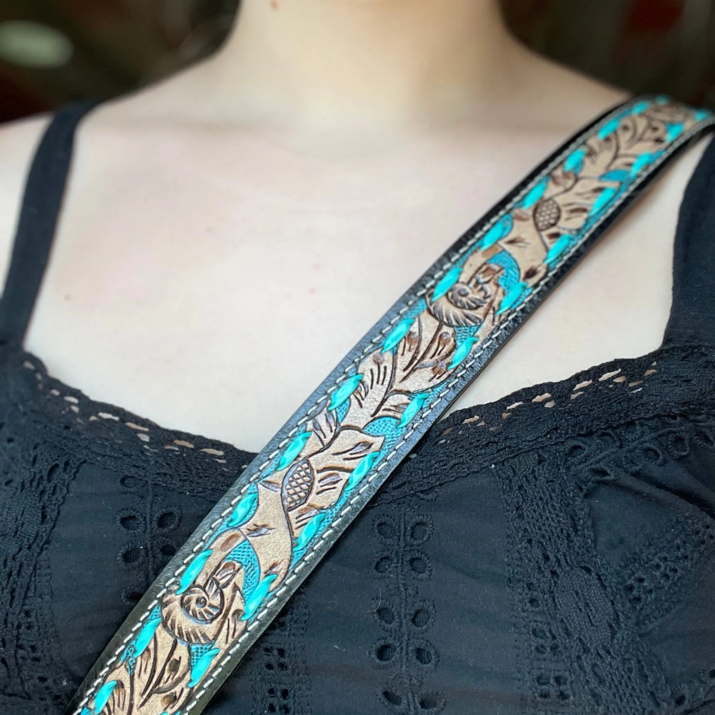 A turquoise and tan leather guitar strap with intricate floral tooling along its length.