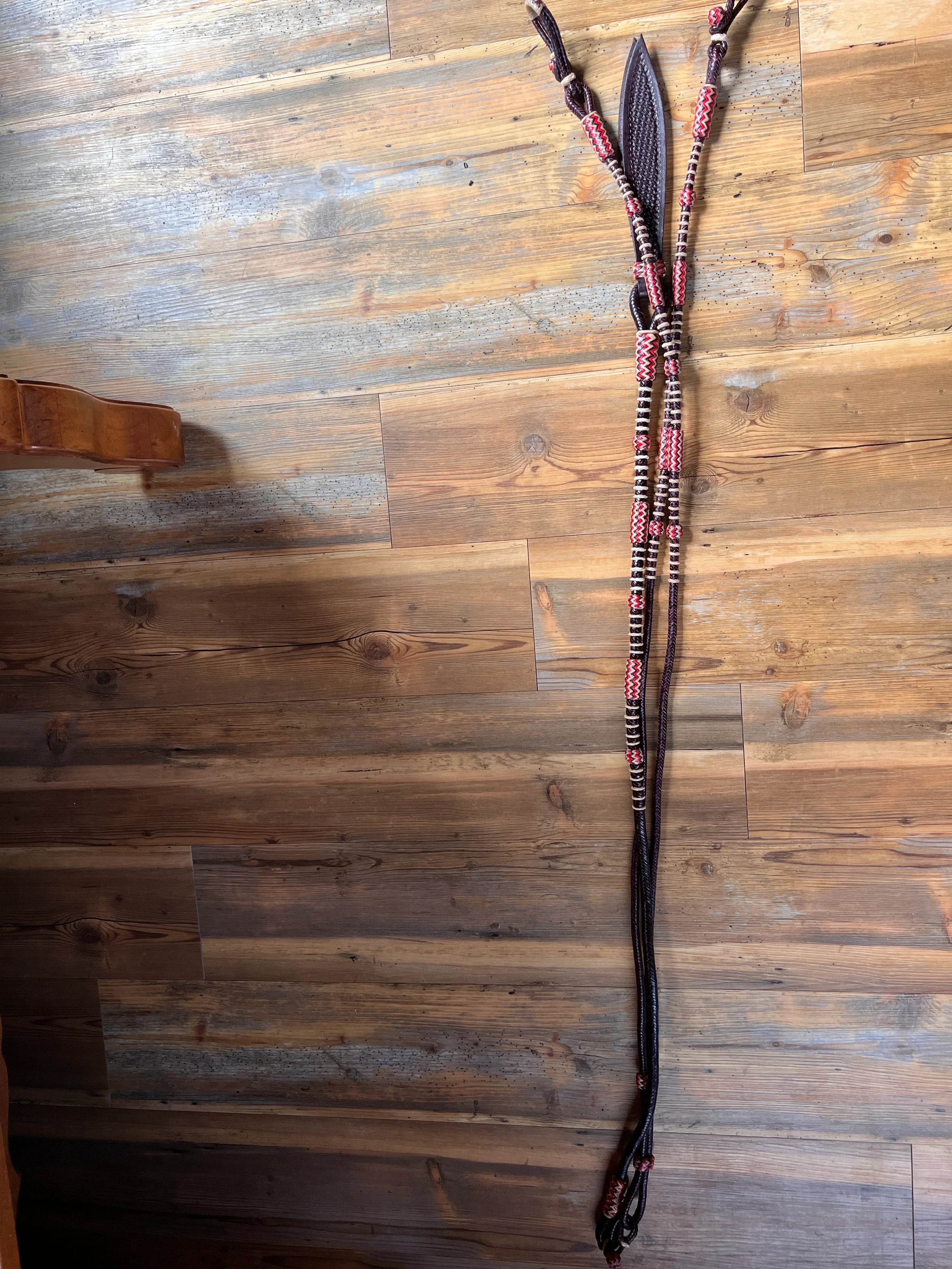 Black leather horse bridle with red white braided accents and romal reins connectors
