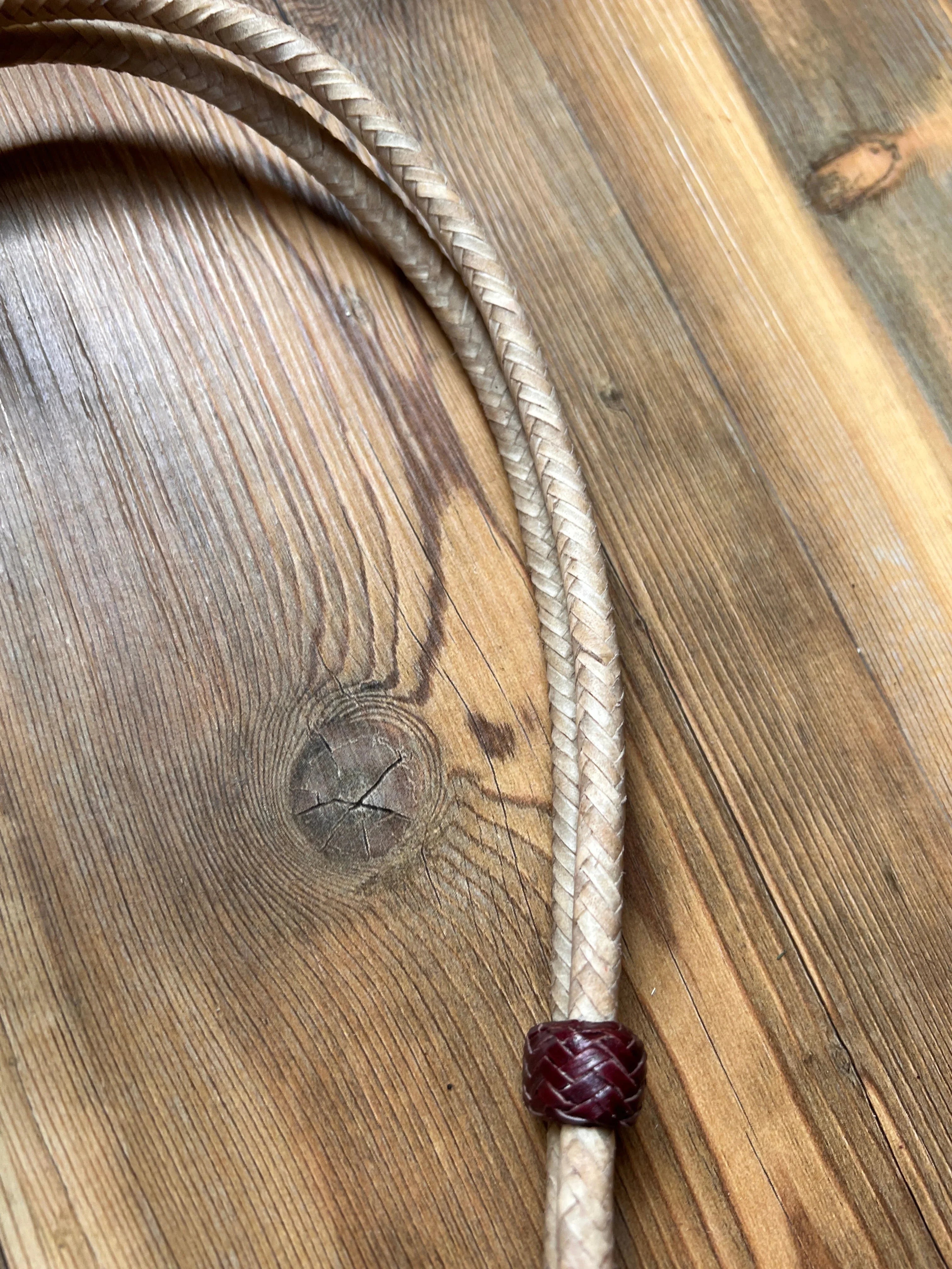Braided light beige leather lanyard with dark red woven bead on natural rawhide headstall
