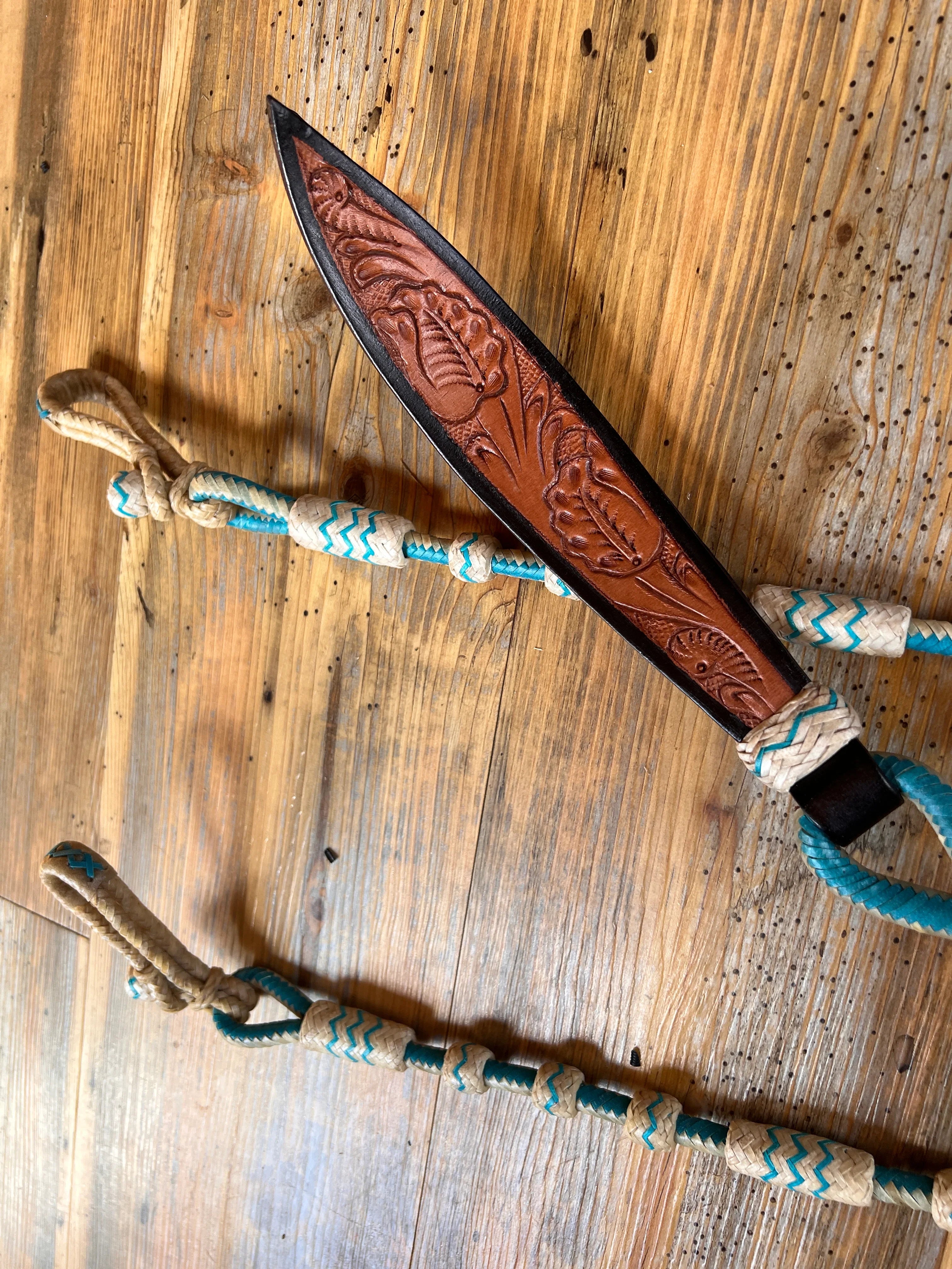 Brown leather knife with floral tooling, black handle, teal beige lanyard on Romal Reins