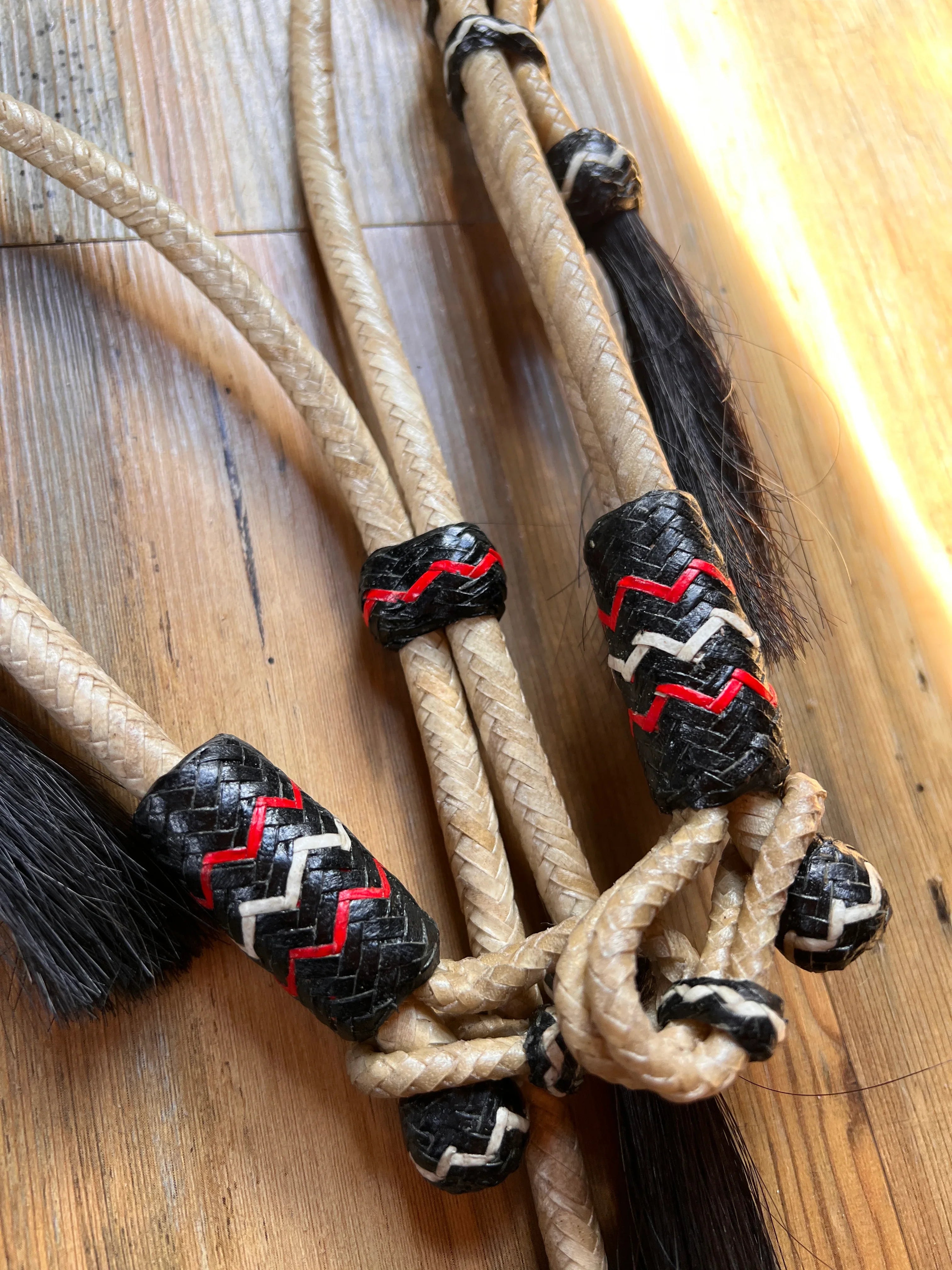 Hand-crafted beige braided rawhide headstall with black accents, zigzag patterns, mane hair tassels